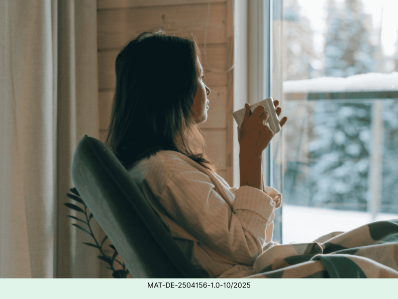 Frau sitzt mit einer Tasse Tee vor einem Fenster und schaut hinaus