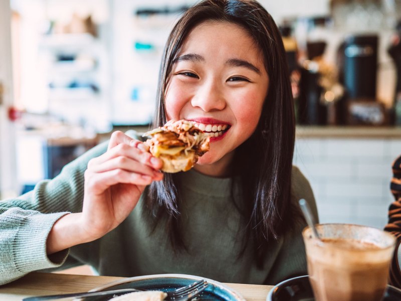 Mädchen im Teenageralter isst eine Pizza und lacht glücklich in die Kamera