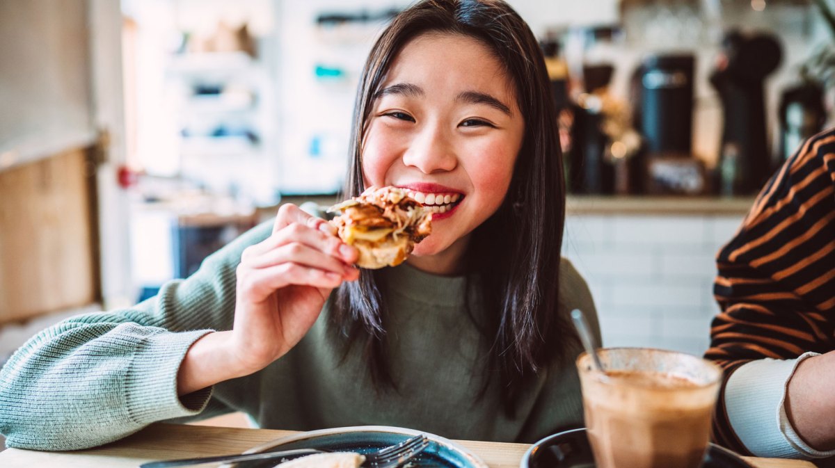 Mädchen im Teenageralter isst eine Pizza und lacht glücklich in die Kamera
