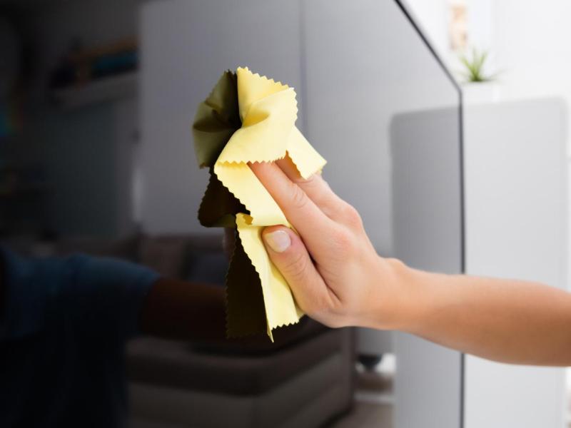 Frau wischt mit einem Mikrofasertuch über den Fernsehbildschirm.