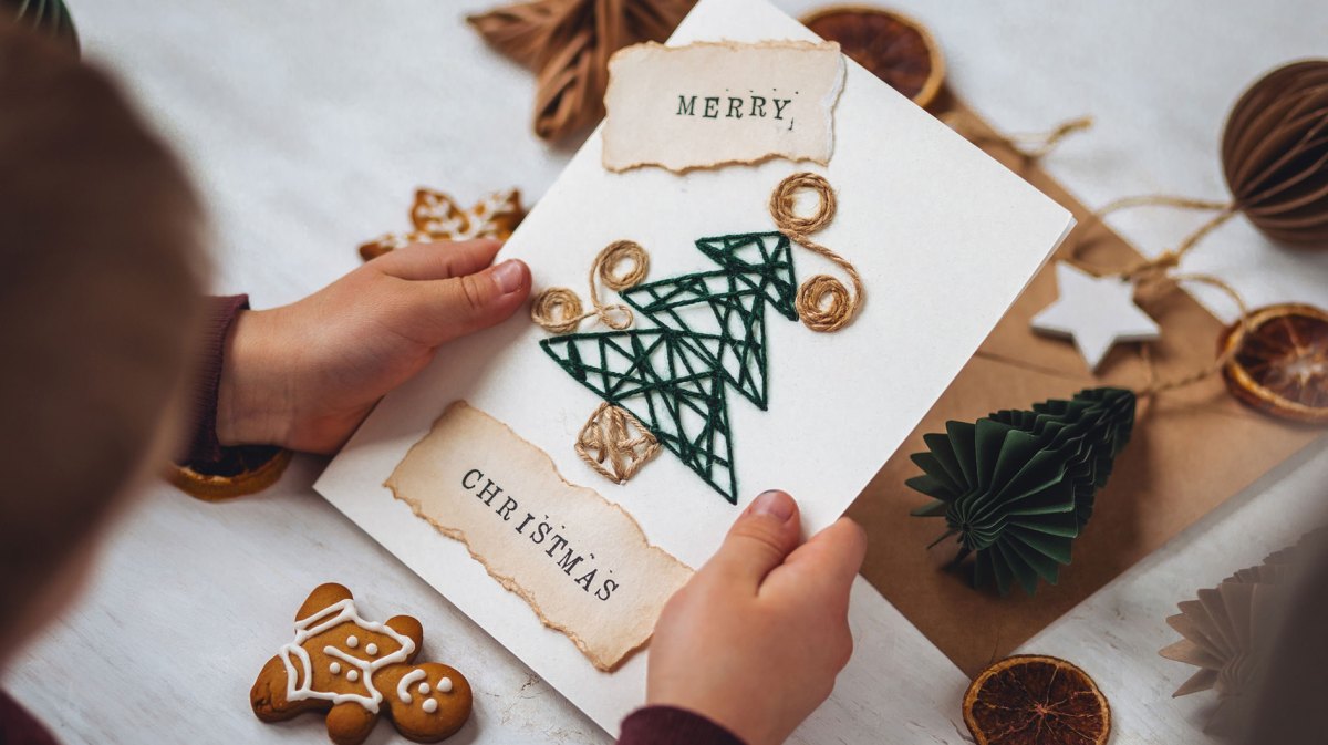 Kinderhände halten eine selbst gebastelte Weihnachtskarte.