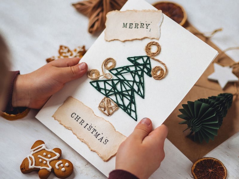 Kinderhände halten eine selbst gebastelte Weihnachtskarte.