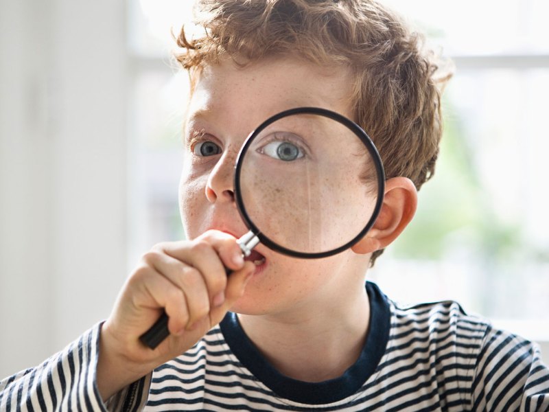 Portr&auml;t eines Jungen, ca. 8 Jahre, der sich eine Lupe vor sein linkes Auge h&auml;lt.
