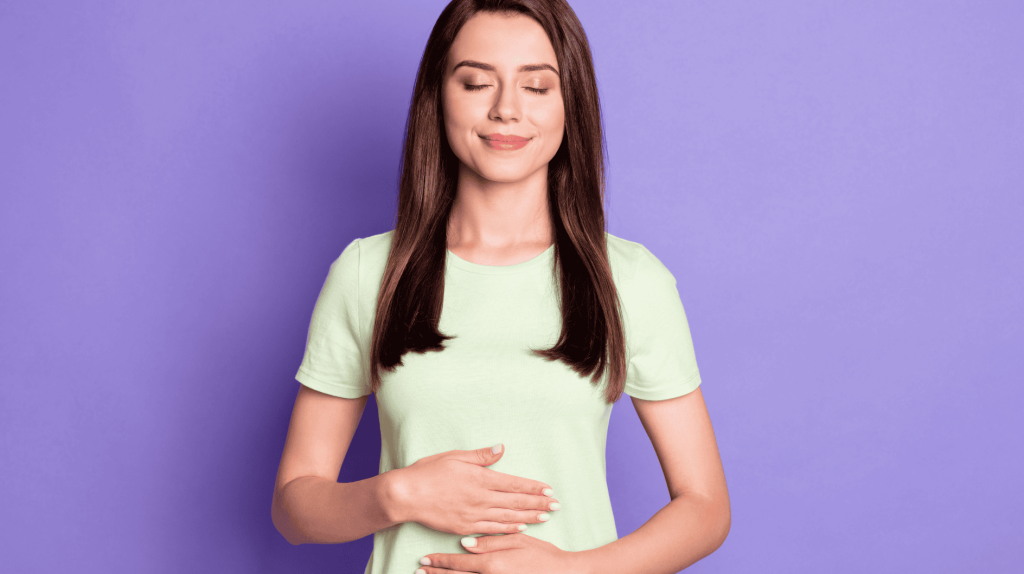 Fotoportr&auml;t eines vertr&auml;umten M&auml;dchens, das nach einem leckeren Fr&uuml;hst&uuml;ck die H&auml;nde auf den Bauch legt und l&auml;chelnd vor einem leuchtend violetten Hintergrund isoliert posiert.&nbsp;