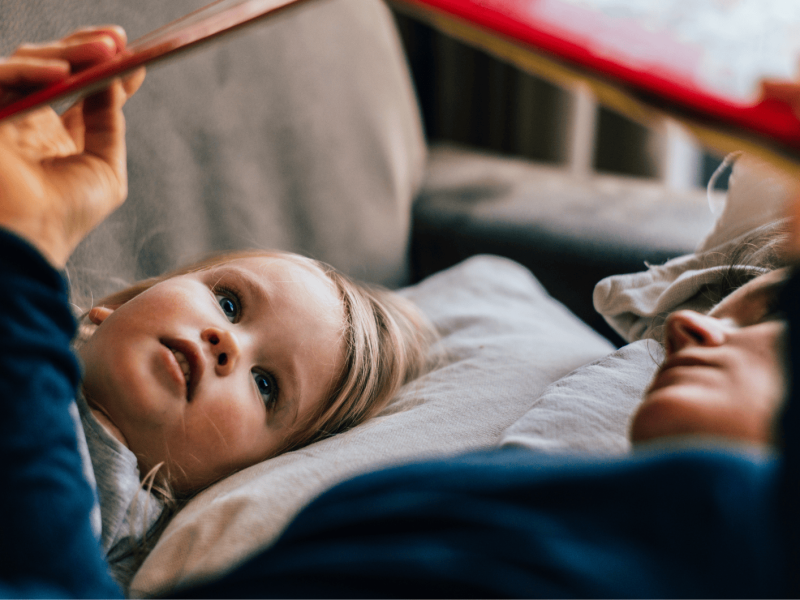 Mutter und Tochter liegen auf der Couch und lesen ein Buch.