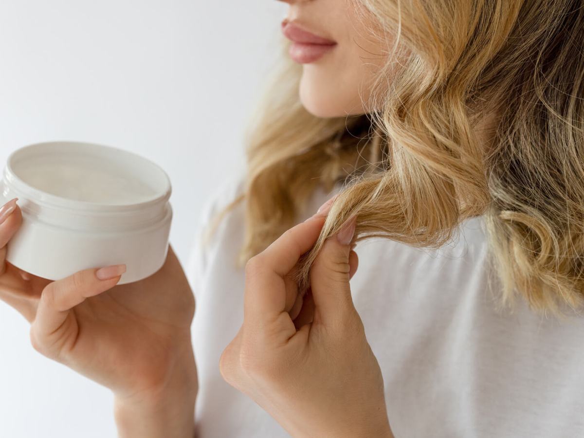 Frau mit blonden, kurzen Haaren gibt sich Haarkur in die Spitzen.