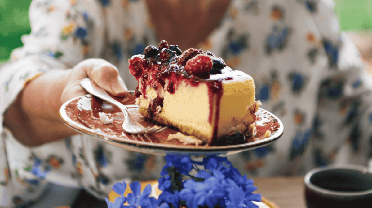Oma reicht über den Tisch ein Teller mit Stück Käsekuchen.