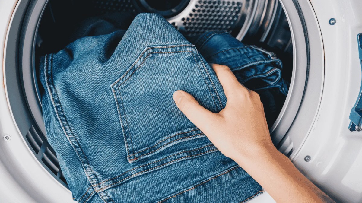 Person gibt Jeans in Waschmaschine.