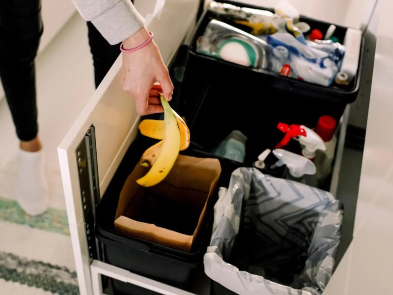 Frau wirft eine Bananenschale in einen Mülleimer in der Küche.