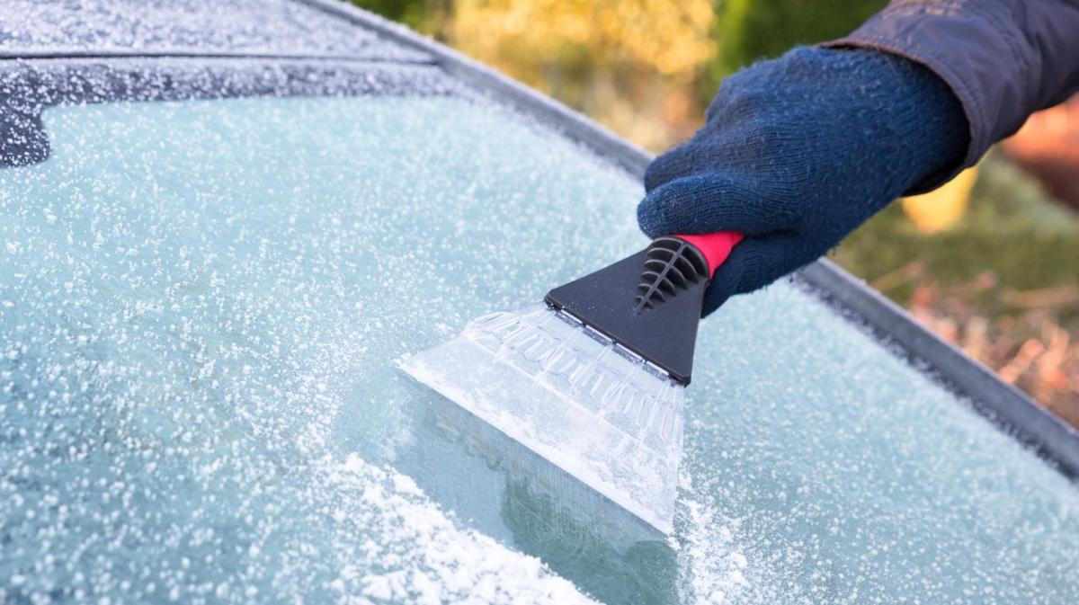 Person kratzt Eis von der Frontscheibe.