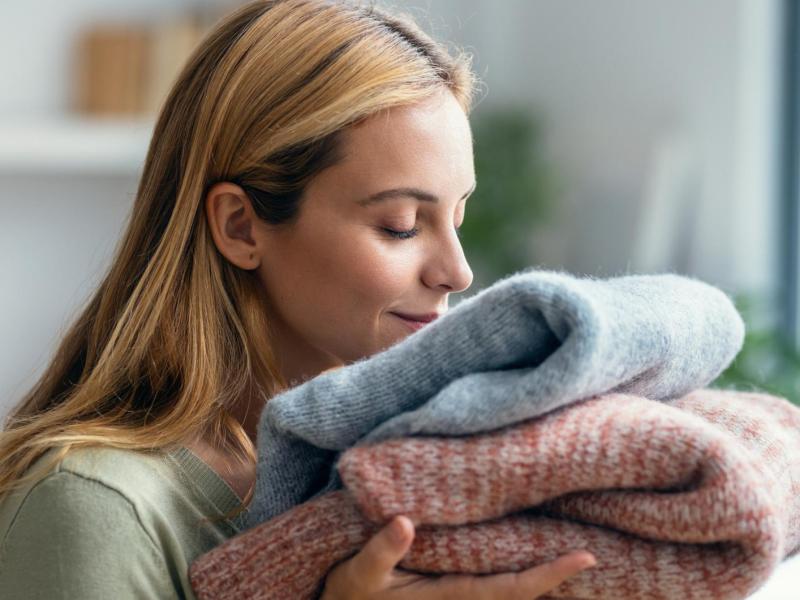Frau riecht an einem Stapel Pullover nach dem Waschen.