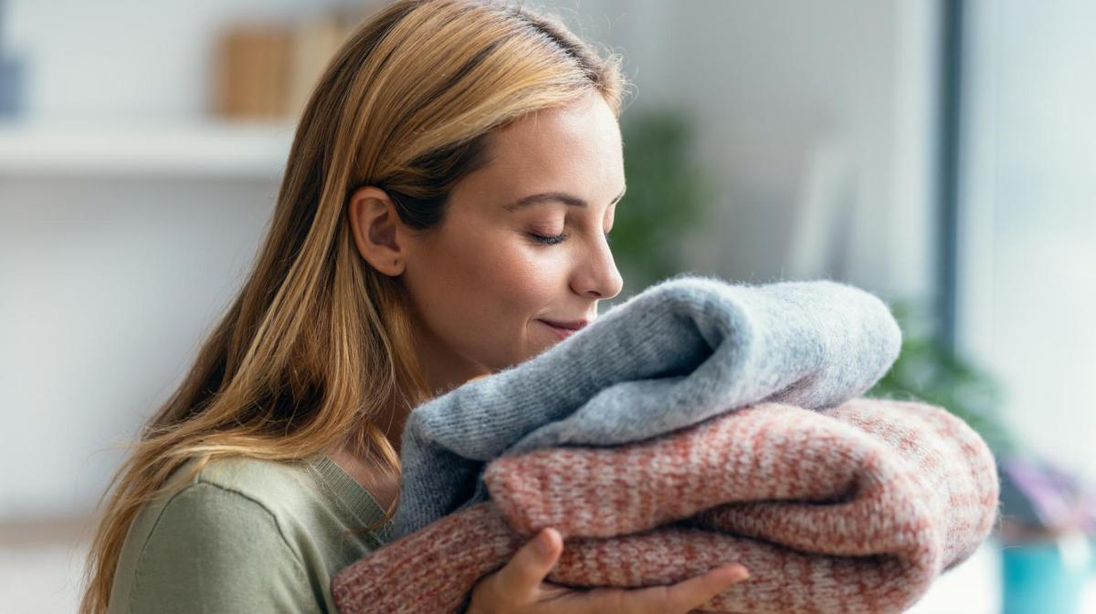 Frau riecht an einem Stapel Pullover nach dem Waschen.