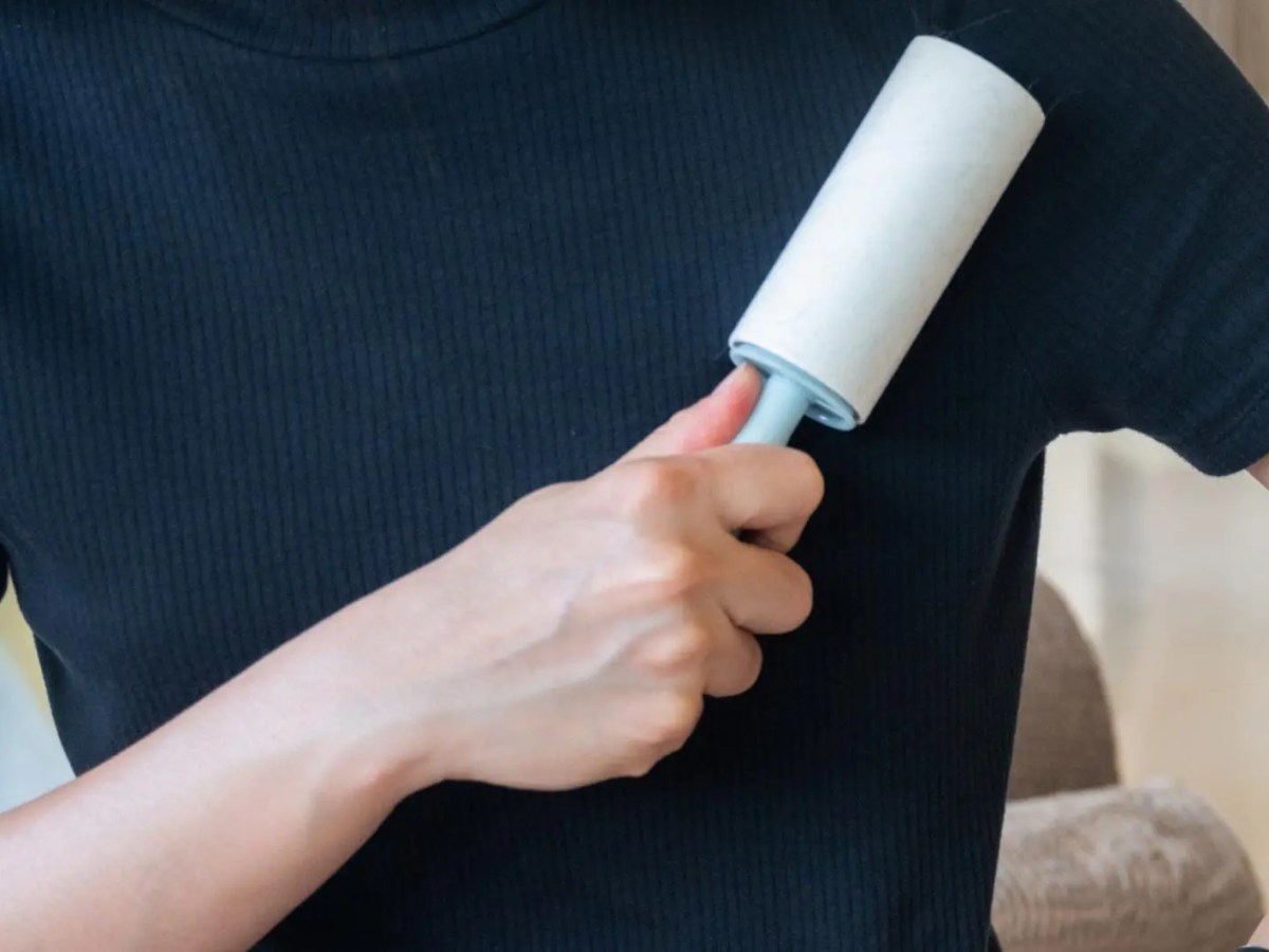 Frau mit einem dunklen T-Shirt streicht mit einer Fusselrolle &uuml;ber die Kleidung.