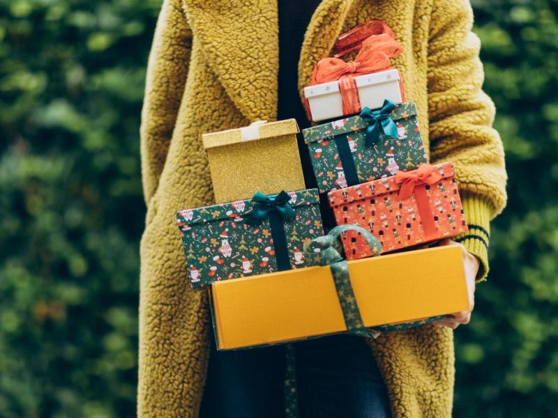Frau mit gelbem Mantel hat viele Geschenke in der Hand.