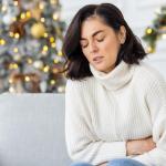 Frau krümmt sich auf der Couch und hält sich den Bauch.