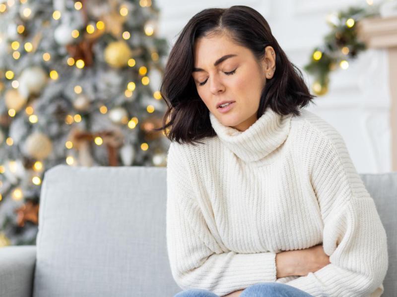 Frau kr&uuml;mmt sich auf der Couch und h&auml;lt sich den Bauch.