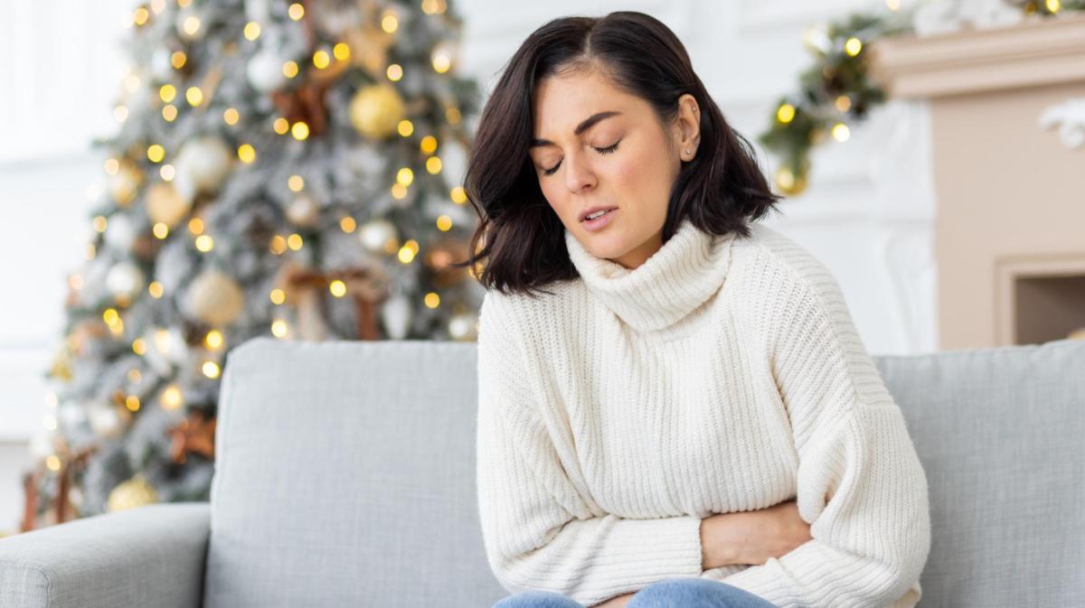 Frau krümmt sich auf der Couch und hält sich den Bauch.