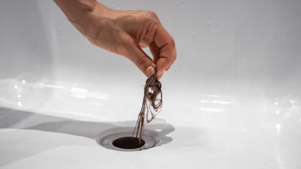Person zieht Haarbüschel aus Abfluss.