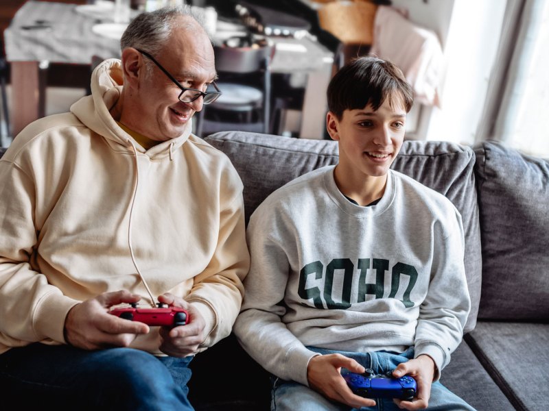 Vater und Teenager-Sohn spielen gemeinsam Playstation im Wohnzimmer.