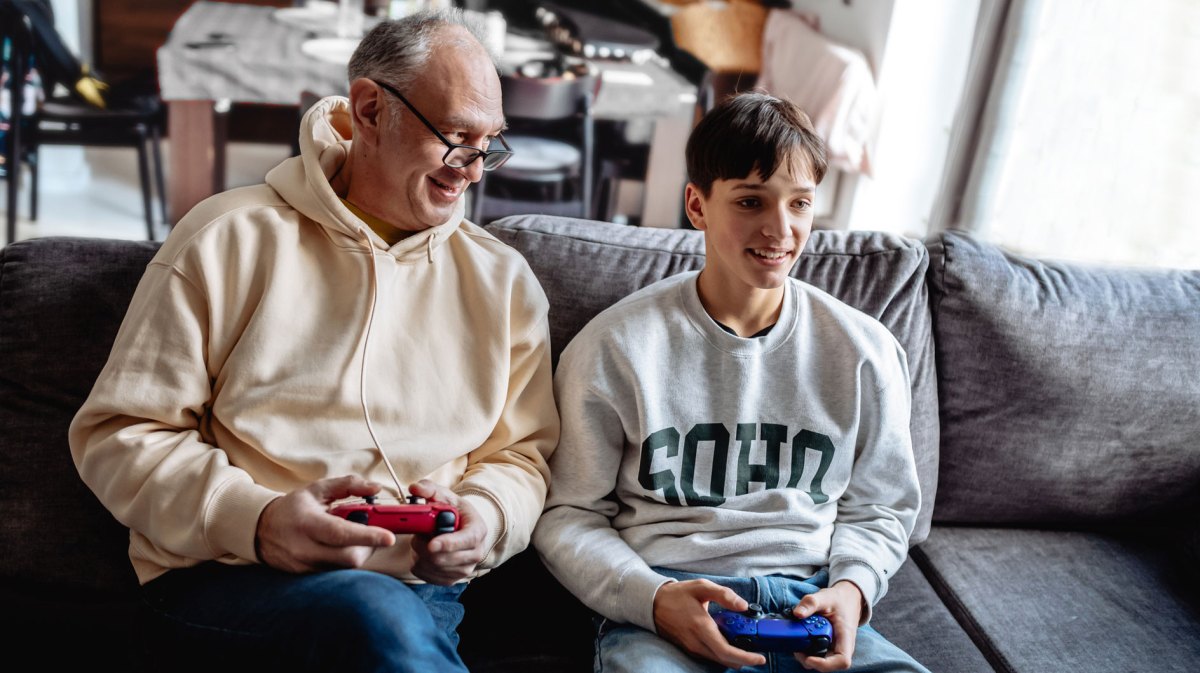 Vater und Teenager-Sohn spielen gemeinsam Playstation im Wohnzimmer.