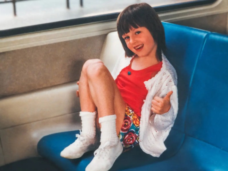 Foto aus den 90ern zeigt ein Mädchen im typischen Look in einer Bahn sitzen.