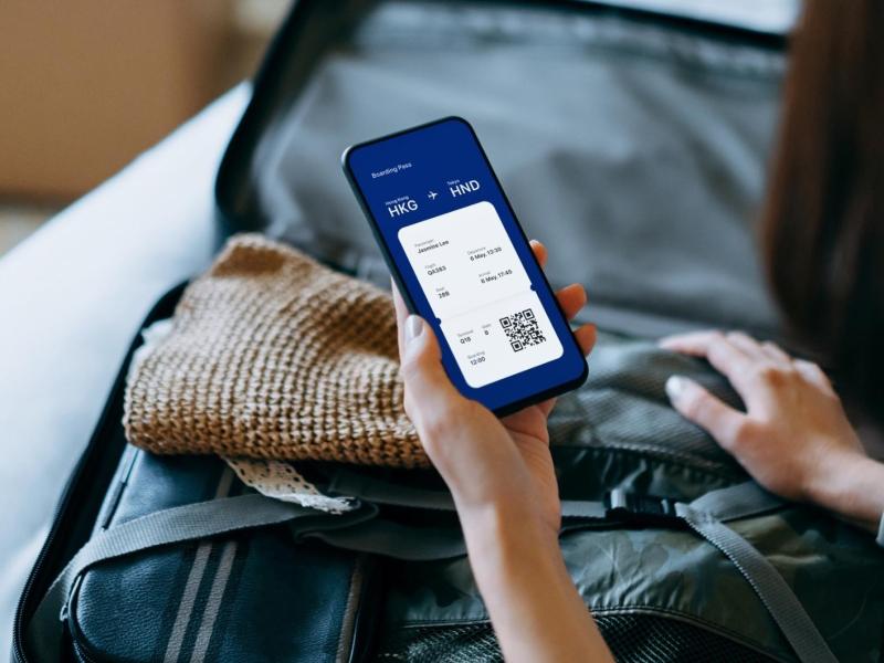 Frau sitzt mit einem gepackten Koffer und einem Handy auf dem Bett.