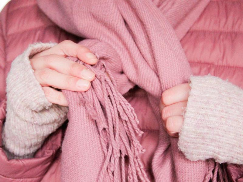 Nahaufnahme von einer Frau mit rosa Jacke, die einen rosa Schal um den Hals bindet.