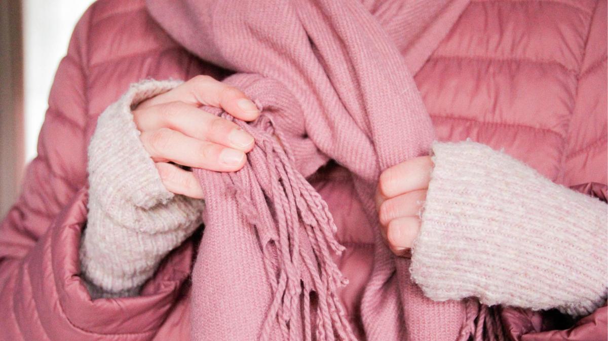 Nahaufnahme von einer Frau mit rosa Jacke, die einen rosa Schal um den Hals bindet.