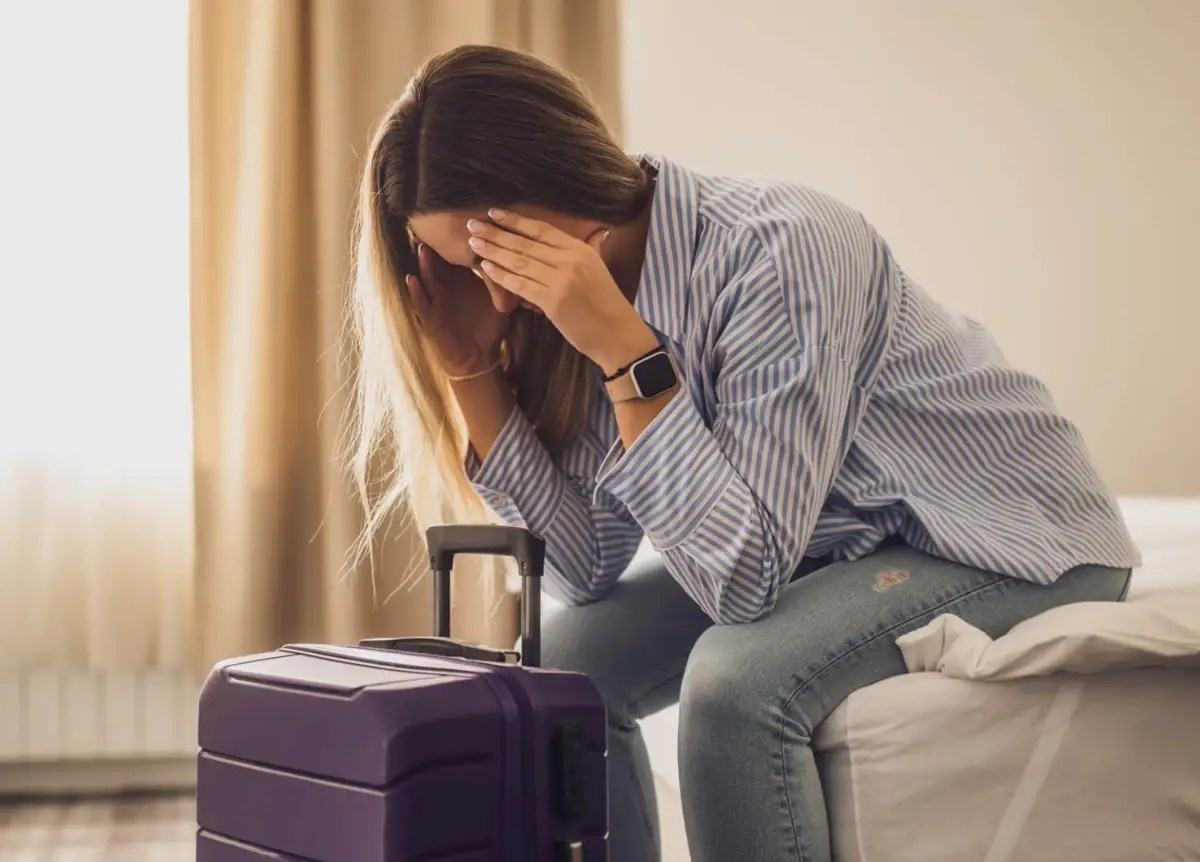 Frau sitzt im Hotelzimmer und hält sich die Hände vors Gesicht