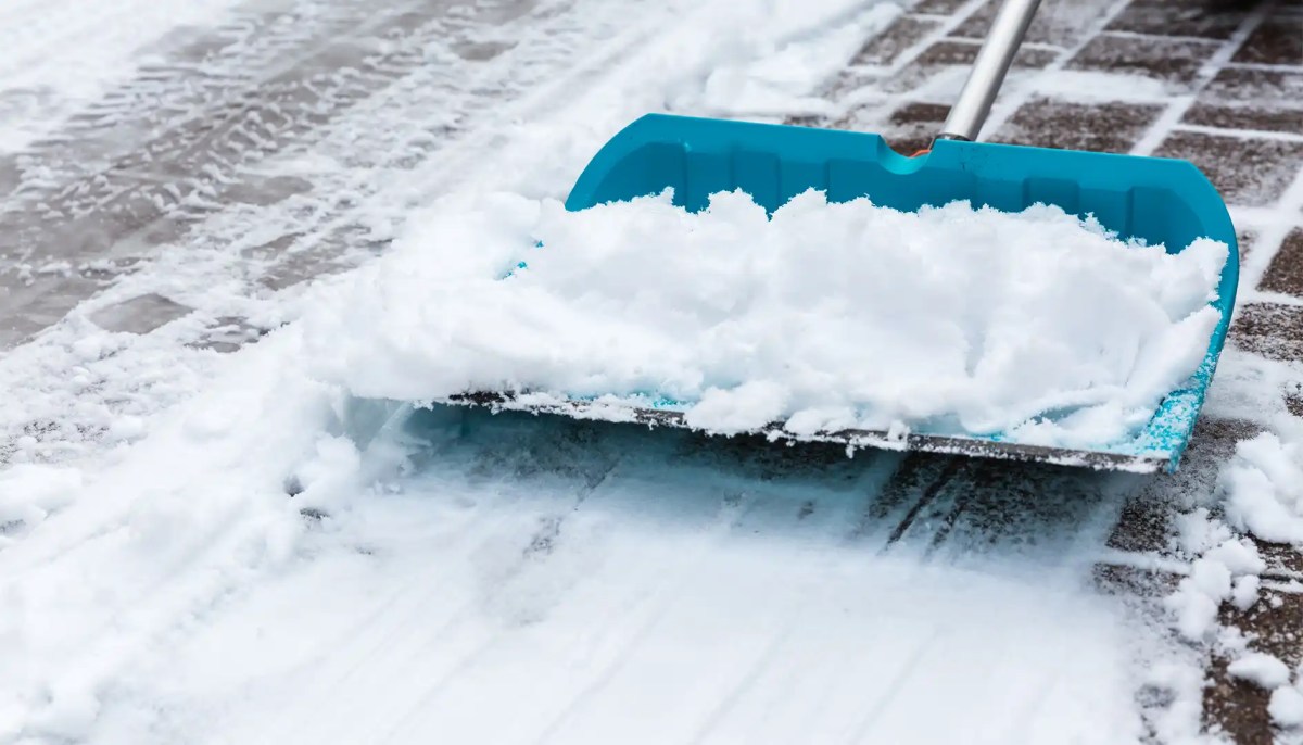 Türkisblauer Schneeschieber befreit den Gehweg von Schnee