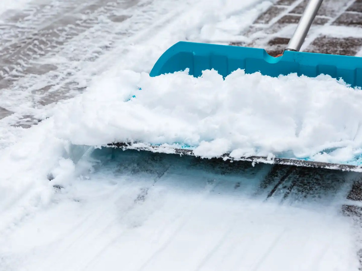 Türkisblauer Schneeschieber befreit den Gehweg von Schnee