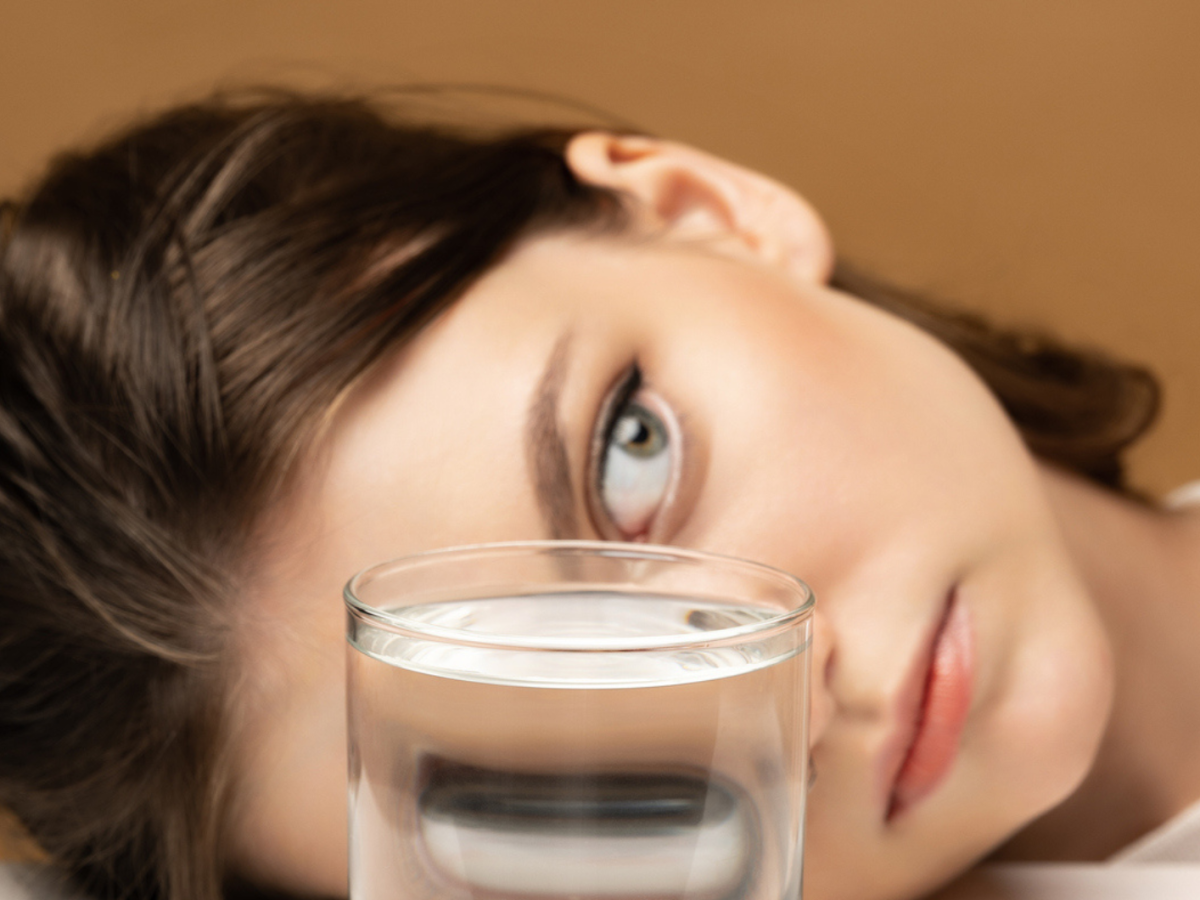 Frau liegt hinter einem Wasserglas, das ihre Gesichtsz&uuml;ge verzerrt