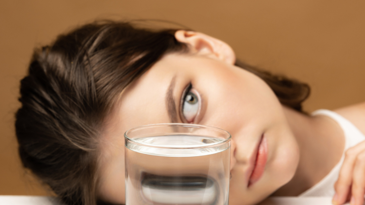 Frau liegt hinter einem Wasserglas, das ihre Gesichtszüge verzerrt