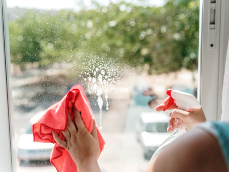 Frau putzt Fenster mit einem feuchten Tuch.