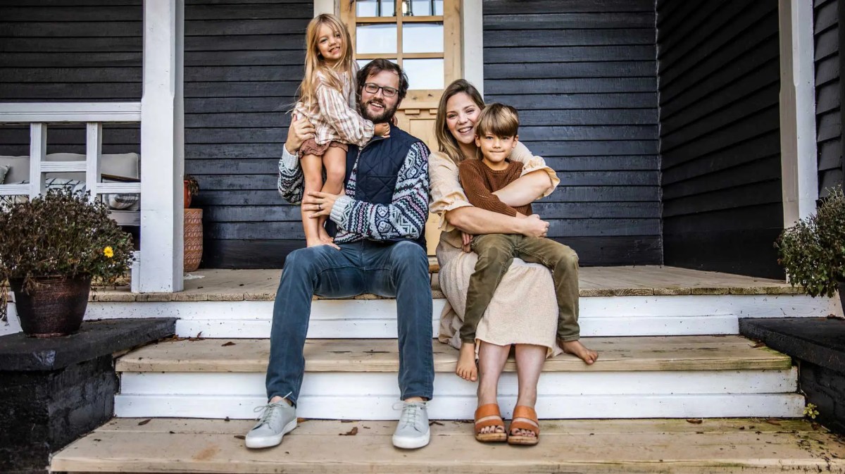 Mutter, Vater und zwei Kinder sitzen auf der Veranda ihres Hauses und posieren für ein Familienfoto.