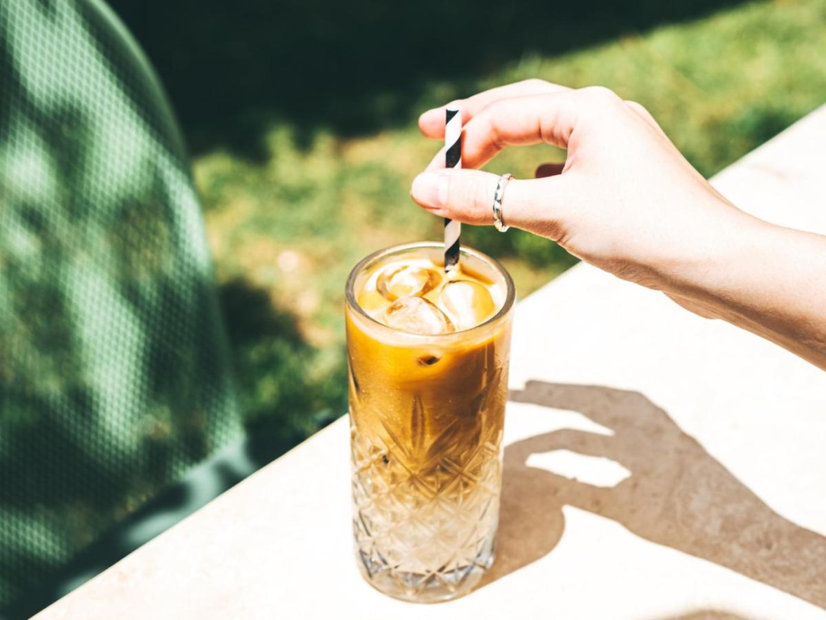 Frau rührt draußen in einem Glas mit Iced Coffee.