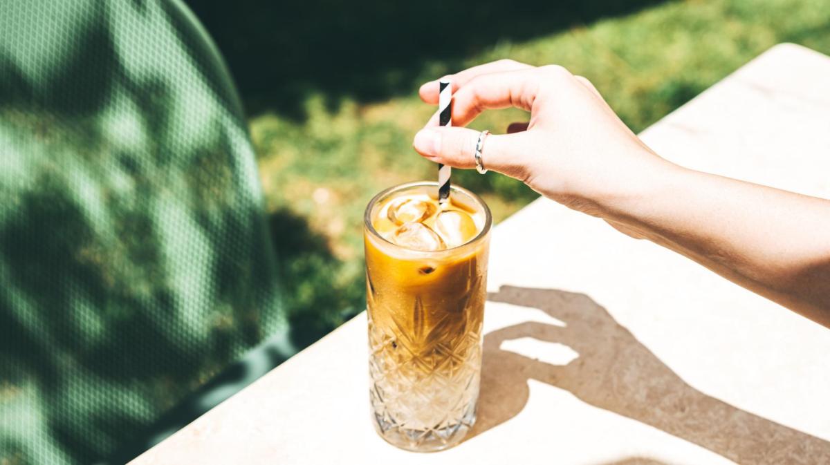 Frau rührt draußen in einem Glas mit Iced Coffee.