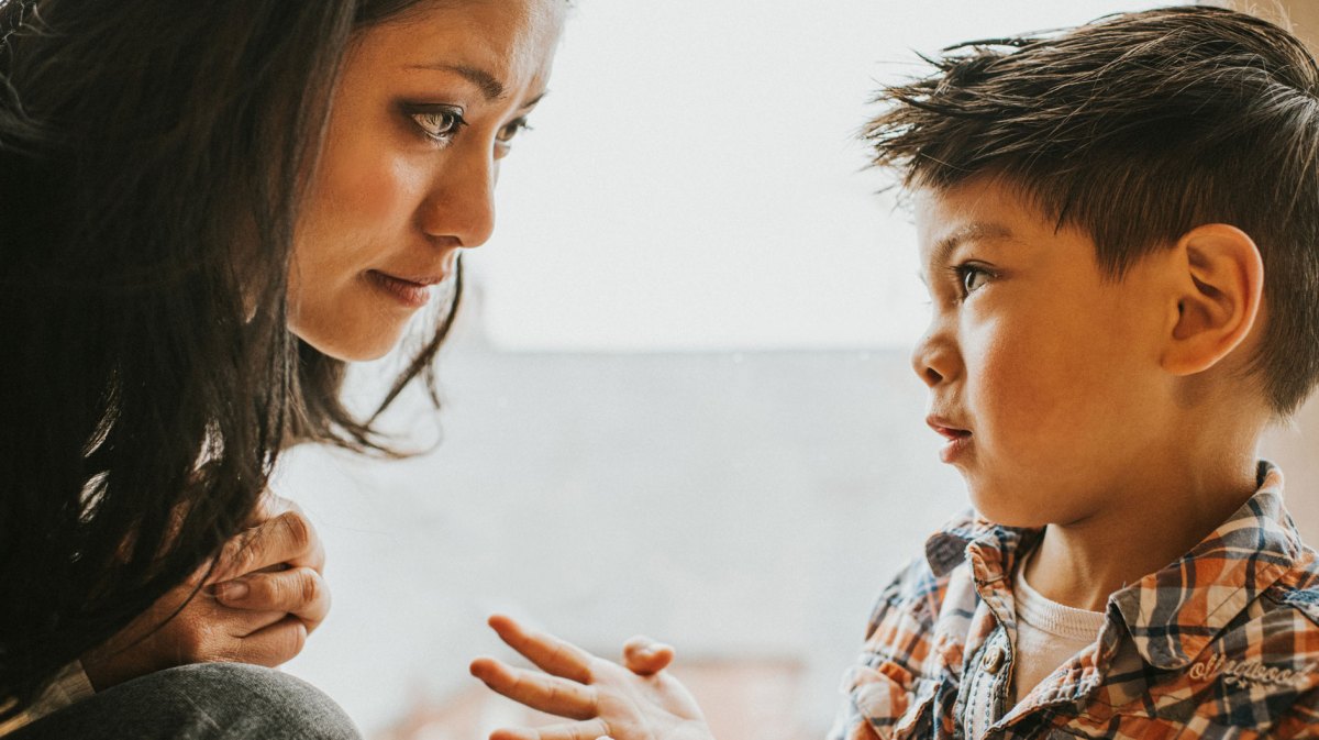 Mutter und Sohn sitzen sich nah bei einander gegenüber und der Sohn schaut seine Mutter bittend an.