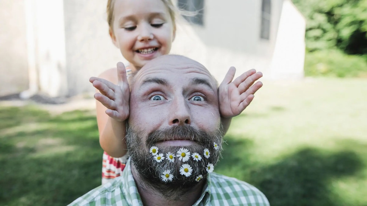Nahaufnahme von Vater, mit Blumen im Bart und Tochter. Beide posieren für die Kamera.