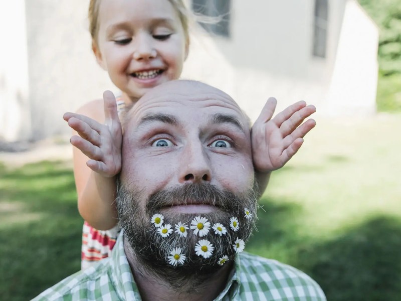 Nahaufnahme von Vater, mit Blumen im Bart und Tochter. Beide posieren für die Kamera.