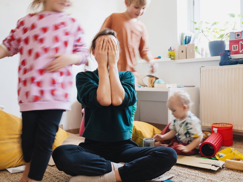 Mutter schl&auml;gt H&auml;nde vors Gesicht, Kinder toben wild um sie herum