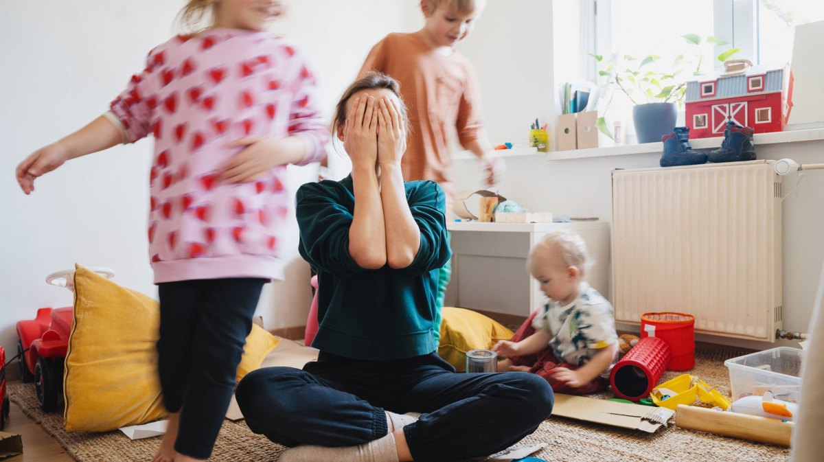 Mutter schlägt Hände vors Gesicht, Kinder toben wild um sie herum