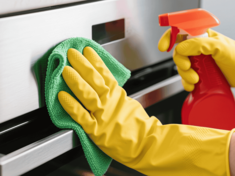 Person wischt mit Lappen &uuml;ber Edelstahl-Backofen.