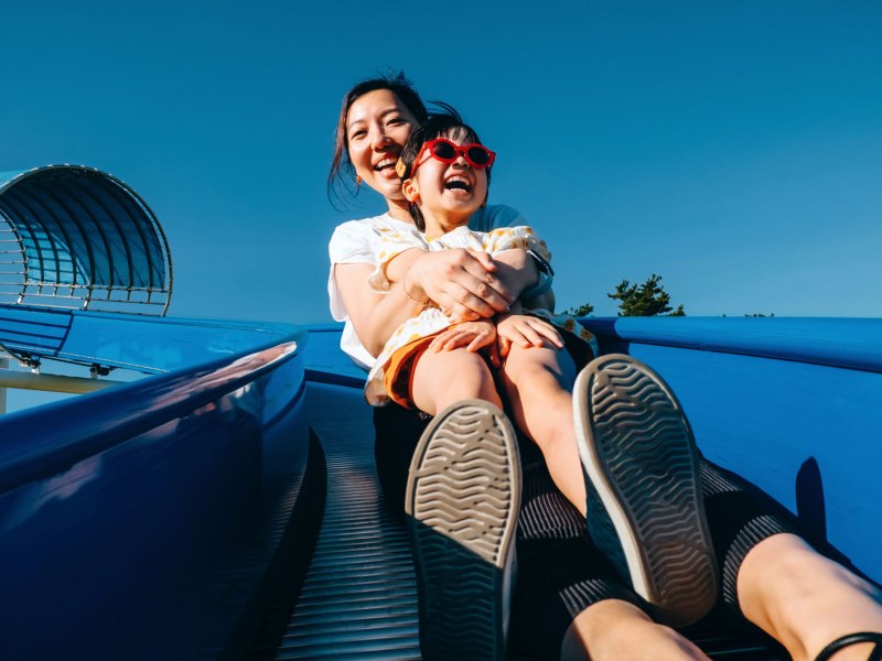 Millenial Mama mit Tochter auf blauer Rutsche