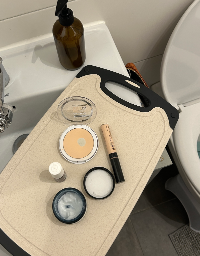 Ein Schneidebrett liegt &uuml;ber ein Waschbecken, darauf verteilt Make-up.