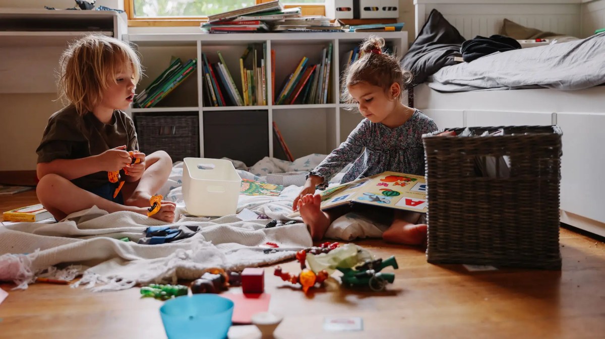 Zwei Kinder sitzen auf dem Fußboden, spielen und lesen.