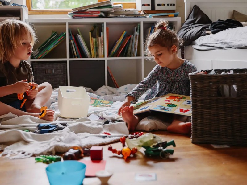 Zwei Kinder sitzen auf dem Fußboden, spielen und lesen.