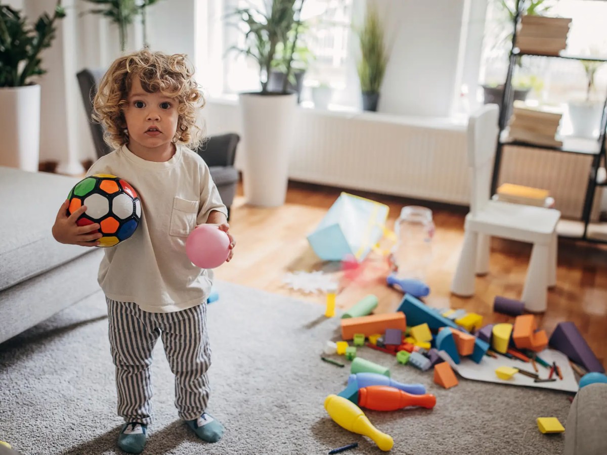 Kind mit Spielzeug in chaotisch wirkendem Wohnzimmer