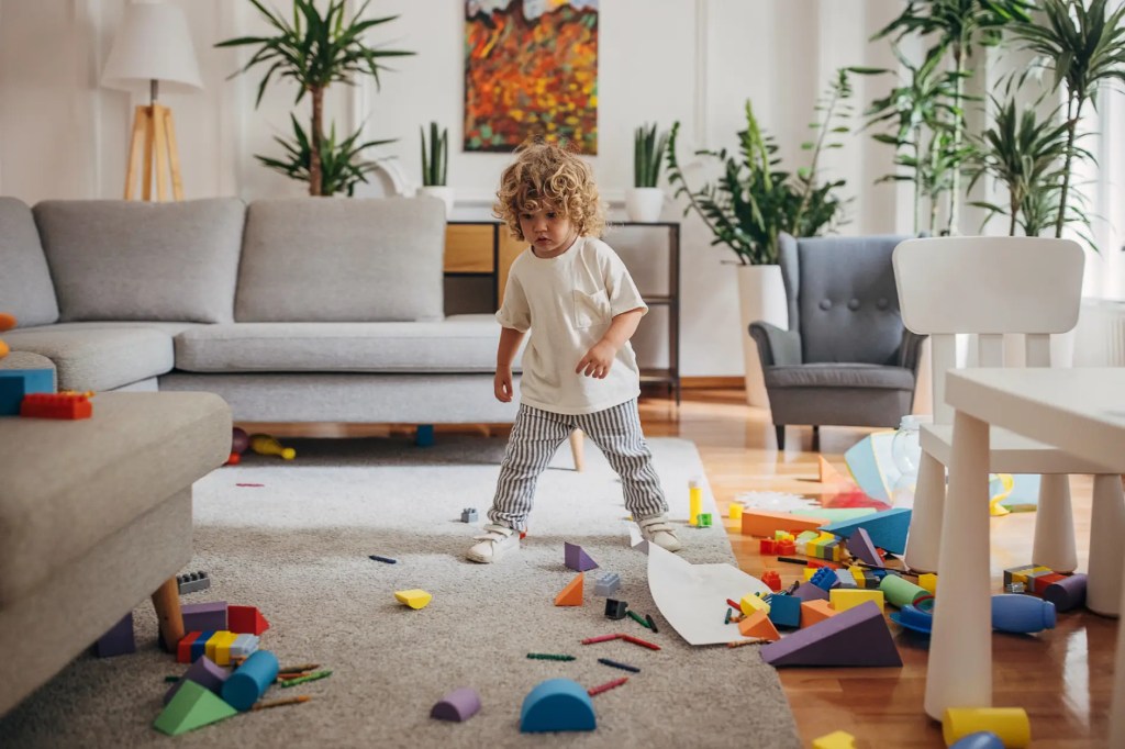 Kleinkind im Wohnzimmer mit verteiltem Spielzeug
