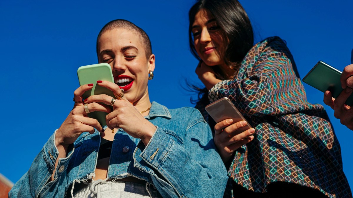 Freundinnen schauen auf ein Smartphone vor einem blauen Himmel
